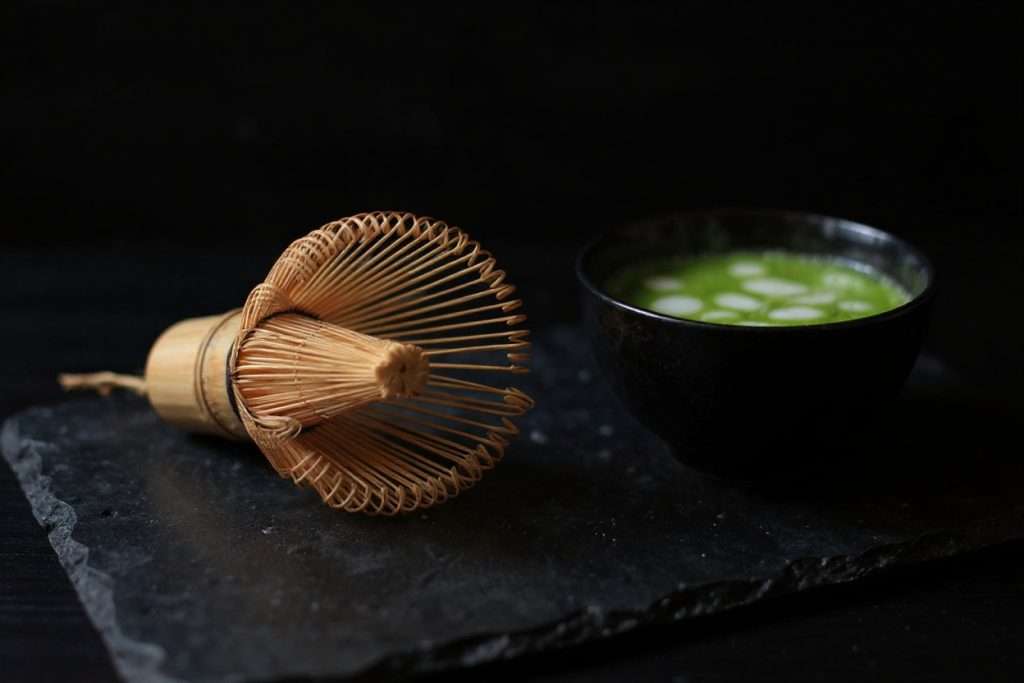 Bol de matcha nature fraîchement fouetté et fouet chasen en bambou sur une ardoise sombre